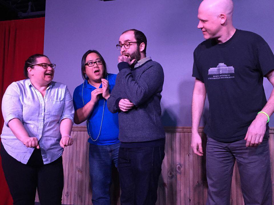 An image of Samuel Dunsiger on stage at the John Candy Box Theatre at Second City Toronto. He is performing an improv scene with three other people and he is looking panicked.